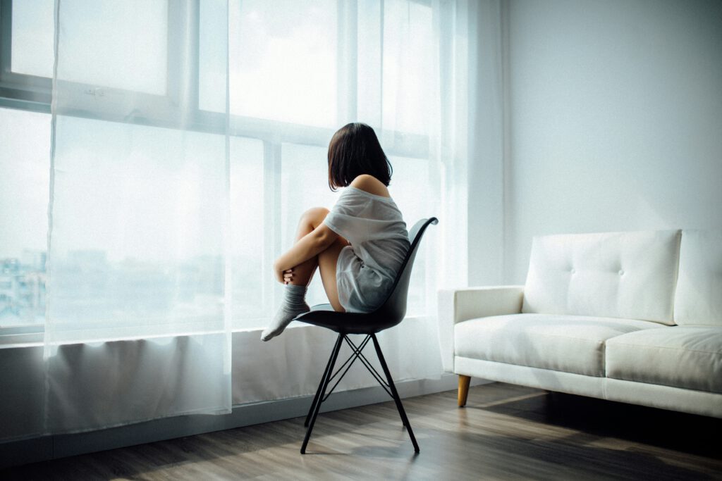 Mujer mirando por la ventana con expresión melancólica, simbolizando el dolor invisible en el autismo.